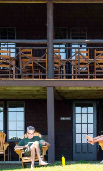 Two people relaxing on lawn chairs in front of a lodge.